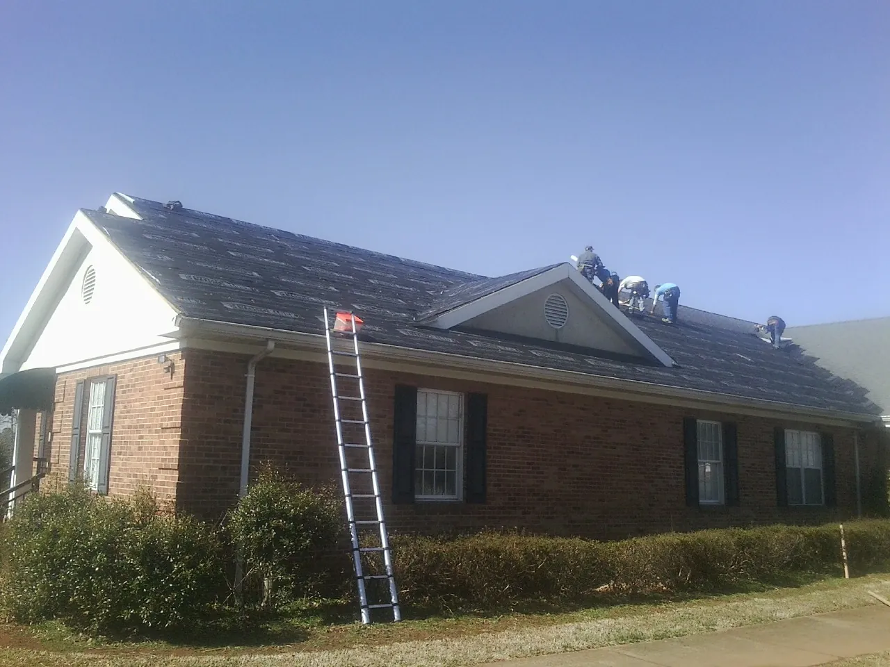 Crew tearing shingles off a brick ranch roof with a ladder set — Emergency Roof Repair work by our crew in Annandale